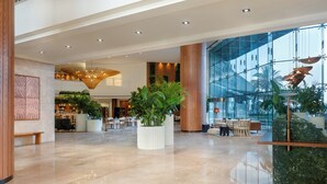 A spacious lobby with a high ceiling, large windows, and a central plant arrangement.