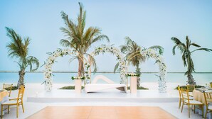 An outdoor wedding venue with a wooden dance floor, white floral arches, and palm trees.
