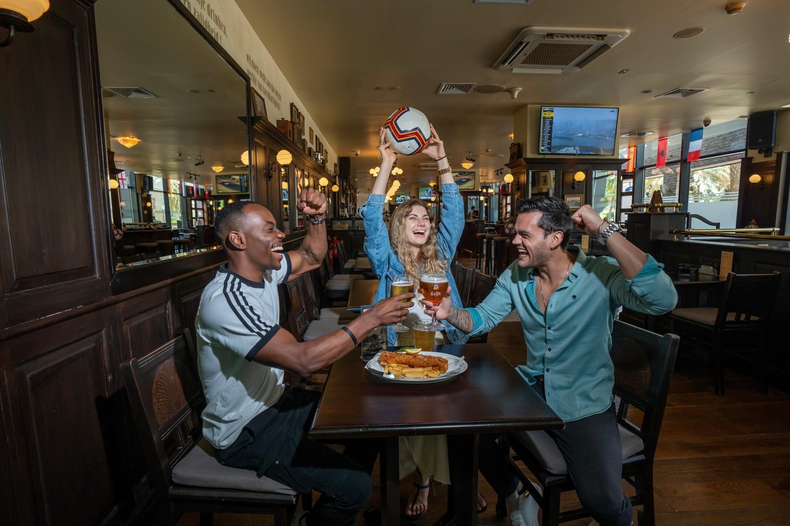Un groupe de personnes est assis à une table dans un restaurant, tenant des boissons et un ballon de sport.