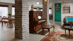Una sala de estar con un piano, columnas de ladrillo, muebles de madera y una puerta verde con un letrero.