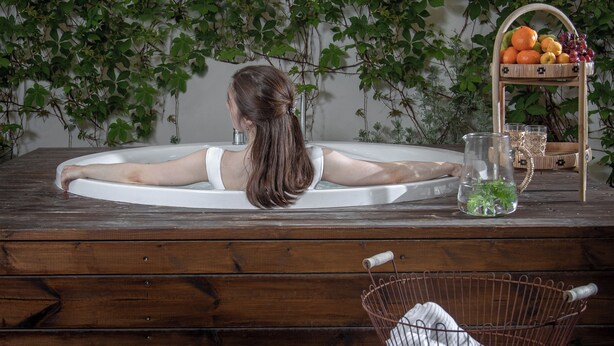 Una mujer se relaja en una bañera con un banco de madera y una cesta de mimbre cerca.