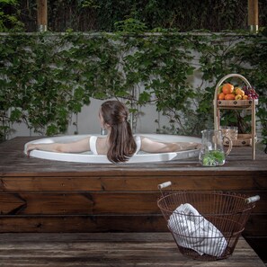 A woman relaxing in a bathtub with a wooden bench and a wicker basket nearby. - Shtarkman Erna Hotel (Nahariya)