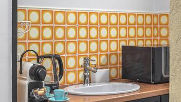 A bathroom with a sink, a coffee maker, a microwave, and a tiled backsplash.