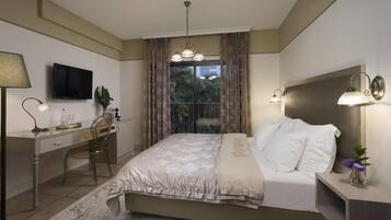 A bedroom with a bed, desk, chair, TV, and a window with curtains.