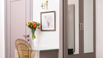 A room with a white cabinet, a glass table with chairs, a vase with flowers, a framed picture, and a large mirror cabinet.