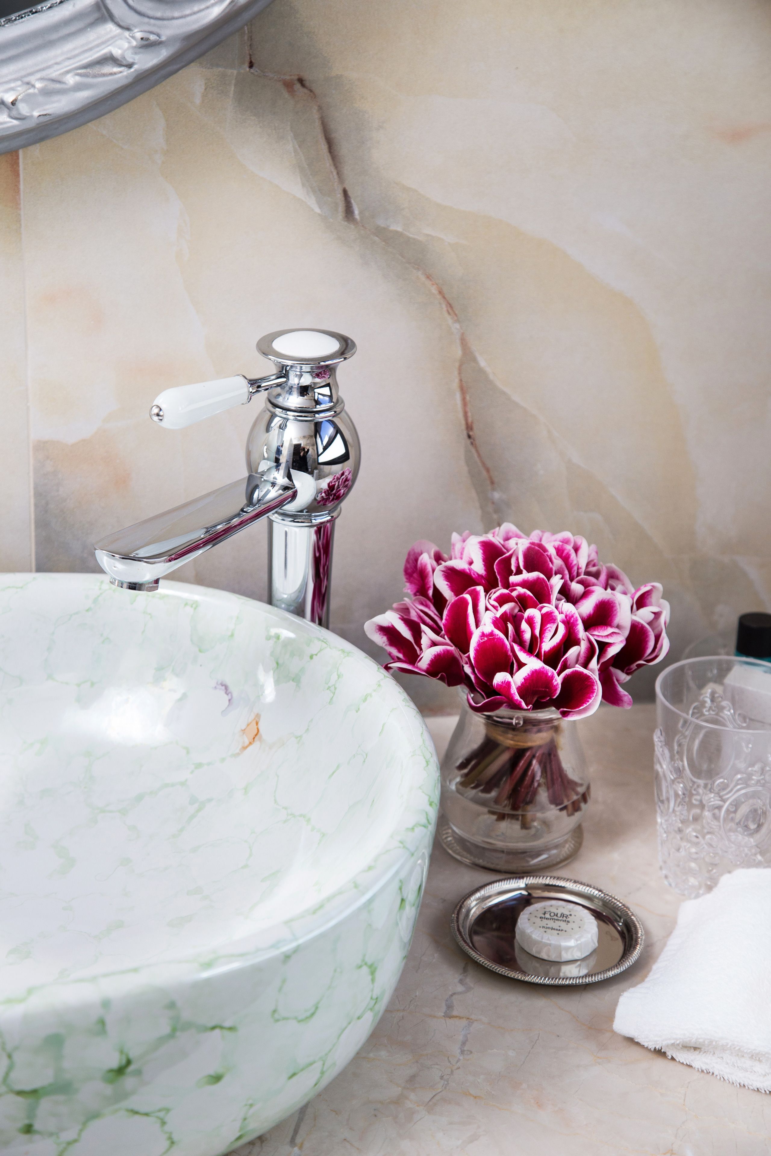 Ein Badezimmer mit einem мраморовым Waschbecken, einem chromfarbenen Wasserhahn und einer Vase mit rosa Blumen.
