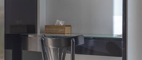 Una habitación moderna con una cama, un escritorio con silla, un espejo y un bote de basura.