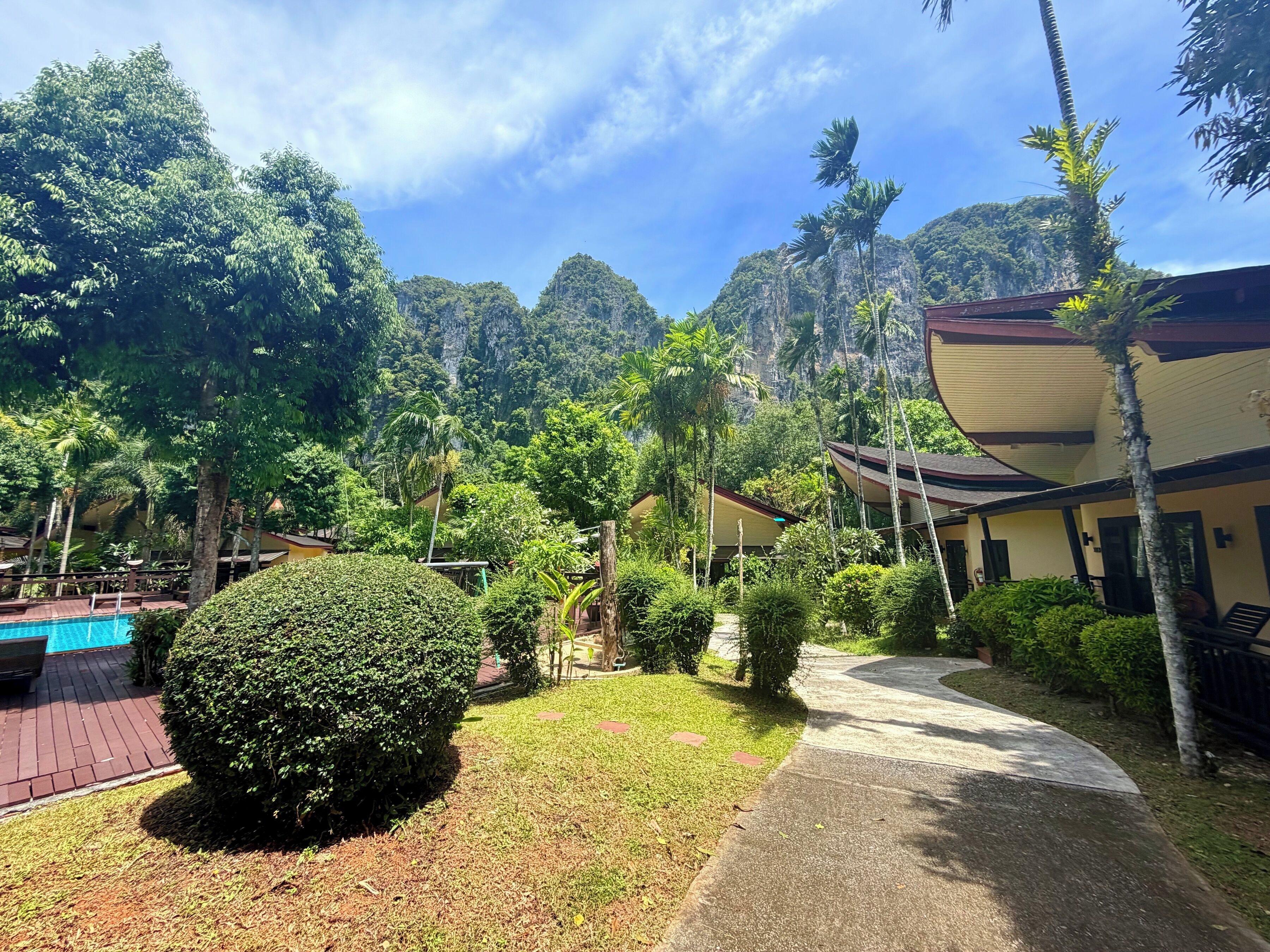 A resort with a swimming pool, lush greenery, and a mountain backdrop.