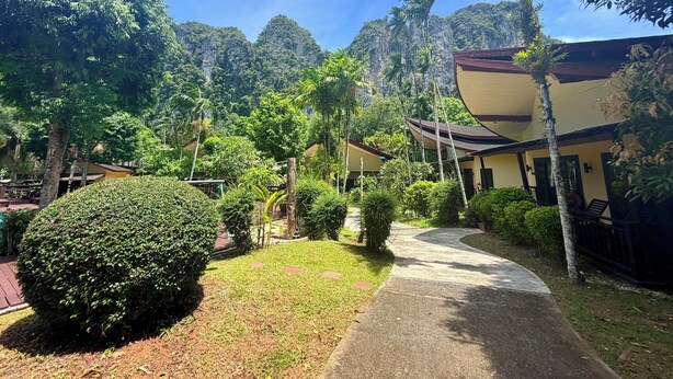 A pathway leading to a building surrounded by lush greenery and a mountainous backdrop.