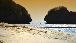 Ein Strand mit freiem Blick auf das Meer und zwei große Felsformationen im Hintergrund.