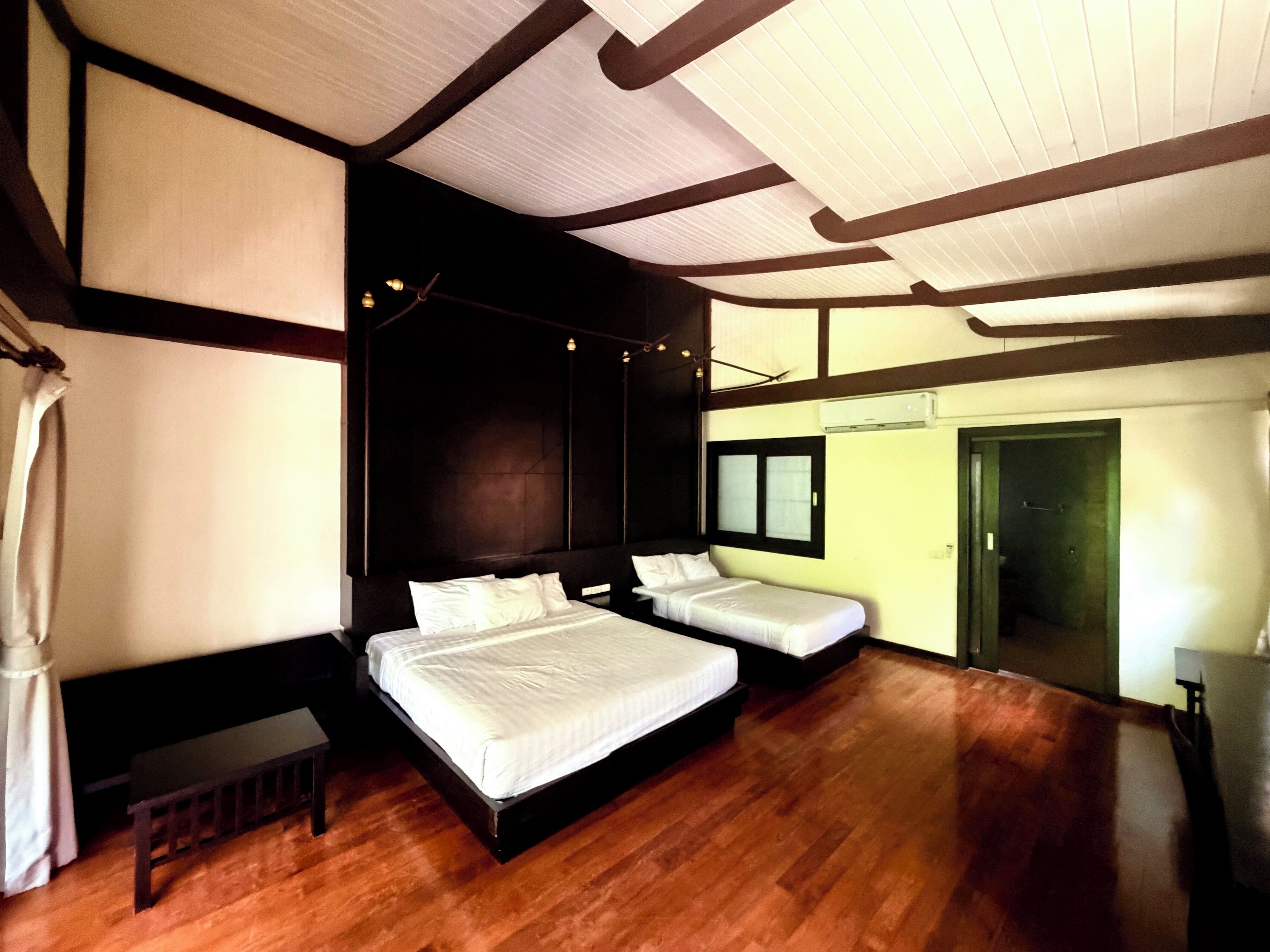 Ein Hotelzimmer mit zwei Betten, Holzboden, großem Fenster und Deckenbalken.