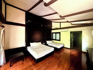 Une chambre d’hôtel avec deux lits, un plancher en bois, une grande fenêtre et un plafond avec des poutres apparentes.