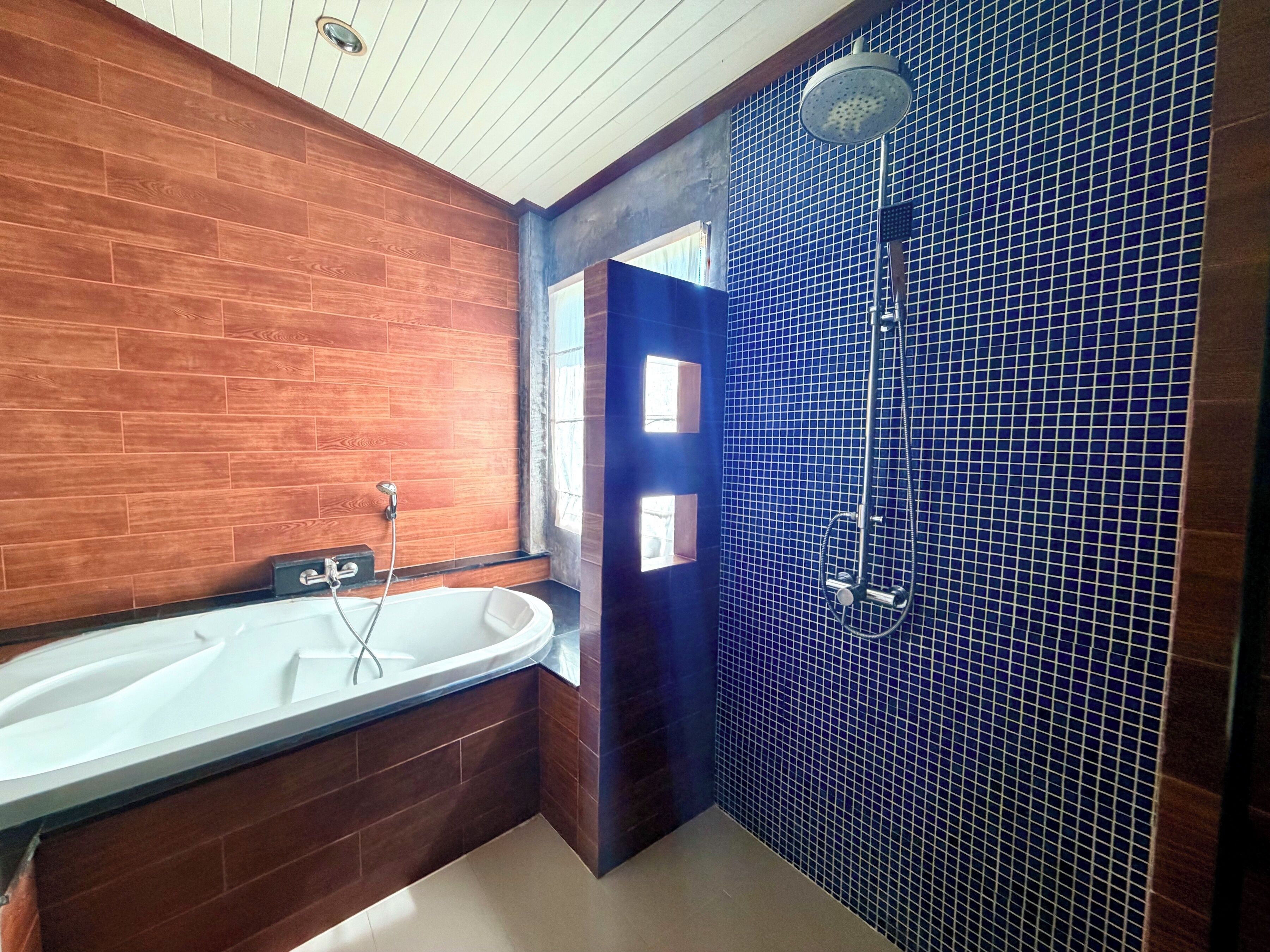 A bathroom with a wooden wall, a white bathtub, and a blue-tiled shower area.