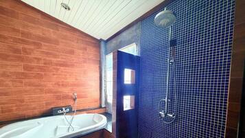 A bathroom with a wooden wall, a white bathtub, and a blue-tiled shower area.