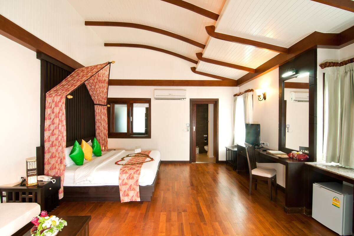 A hotel room with a bed, desk, chair, and a small refrigerator.