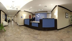 A hotel reception area with a curved reception desk, a receptionist, and a hallway leading to other rooms. - Holiday Inn Express Hotel & Suites Albuquerque Airport by IHG (Albuquerque)