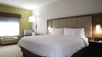 A hotel room with a large bed, a bedside table with a lamp, a chair, and a window with curtains.
