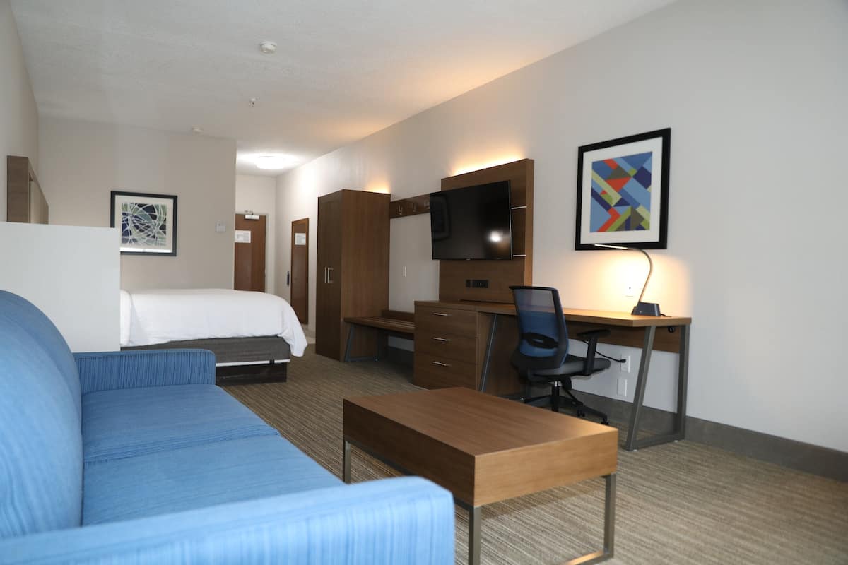 A hotel room with a bed, a blue sofa, a desk with a computer, a chair, and a TV.