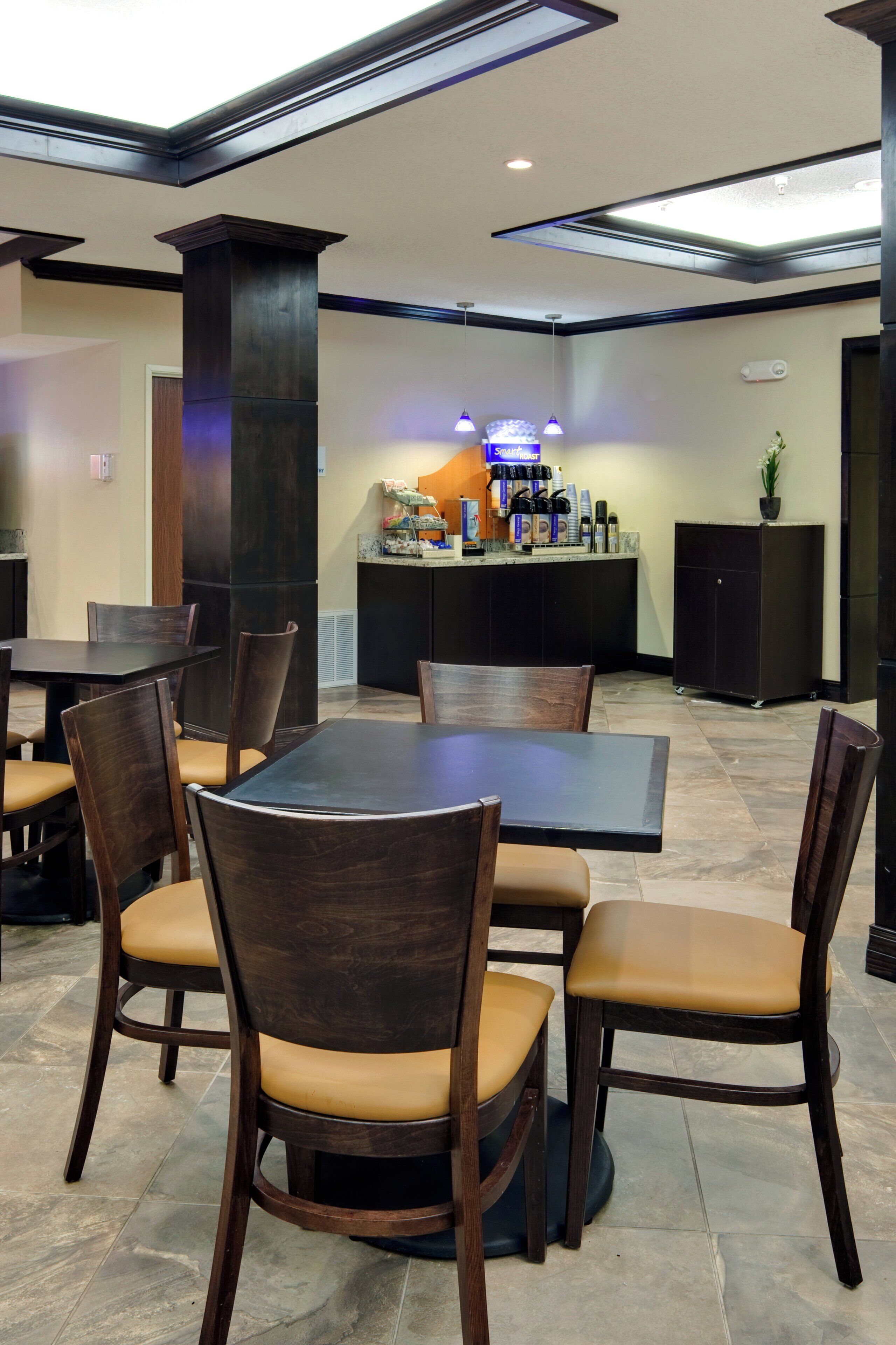 A restaurant with a central dining table surrounded by chairs, a bar area with various items, and a ceiling with recessed lighting.