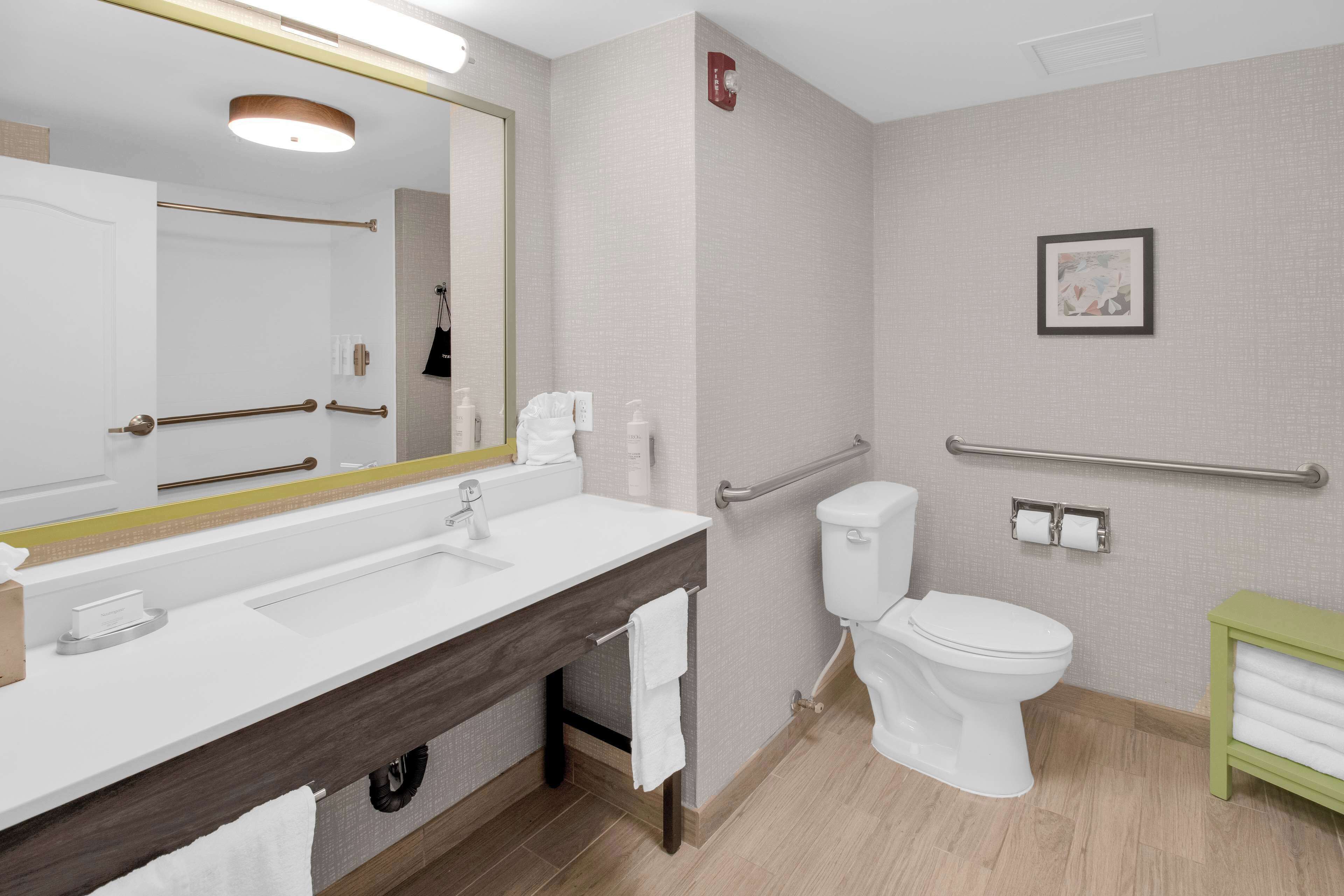 A modern bathroom with a white sink, a toilet, a shower area, and a green towel rack.