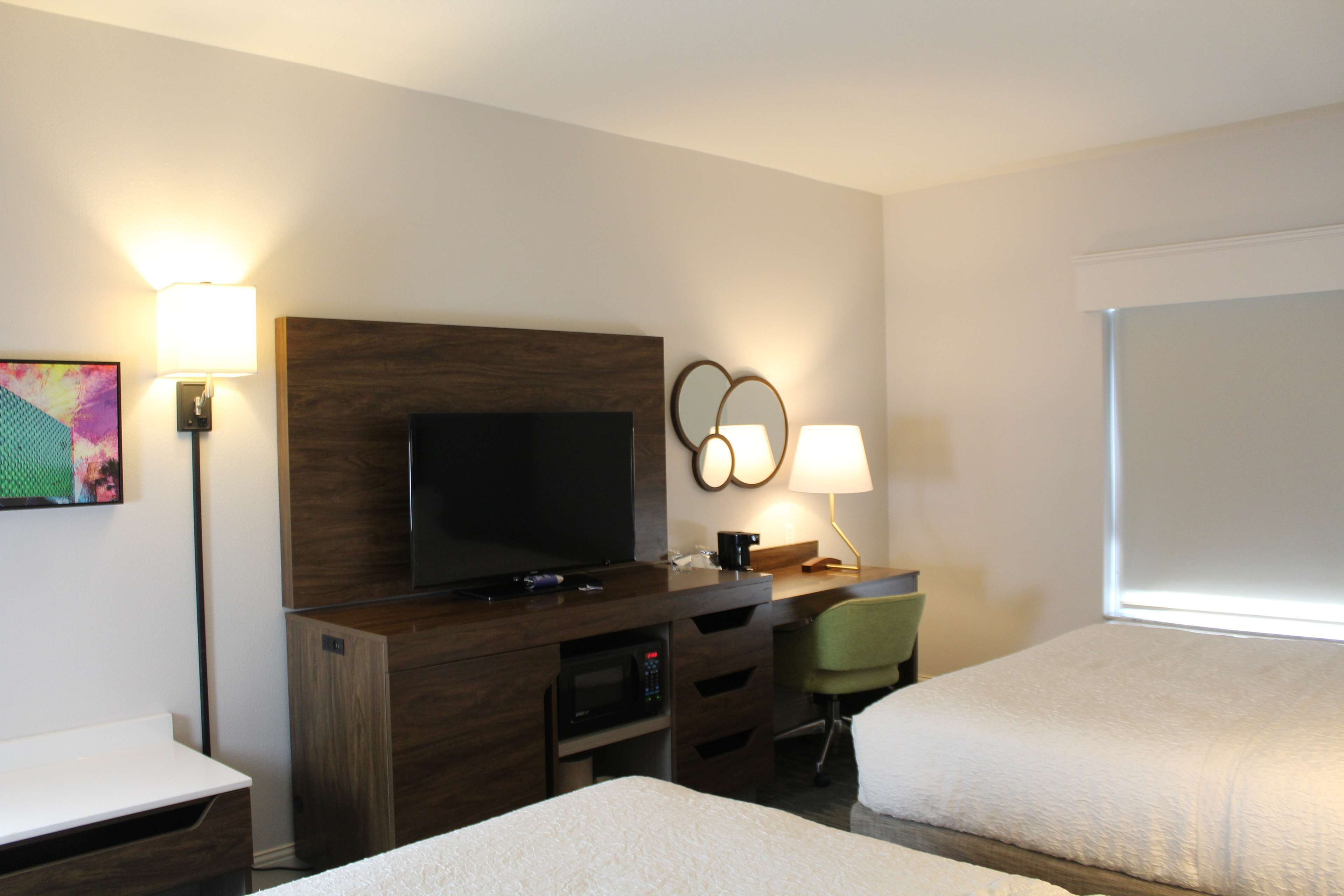 Habitación de hotel con televisión, escritorio, silla y dos camas.