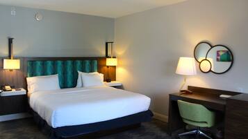 A hotel room with a large bed, two bedside lamps, a desk with a chair, and a wall-mounted artwork.