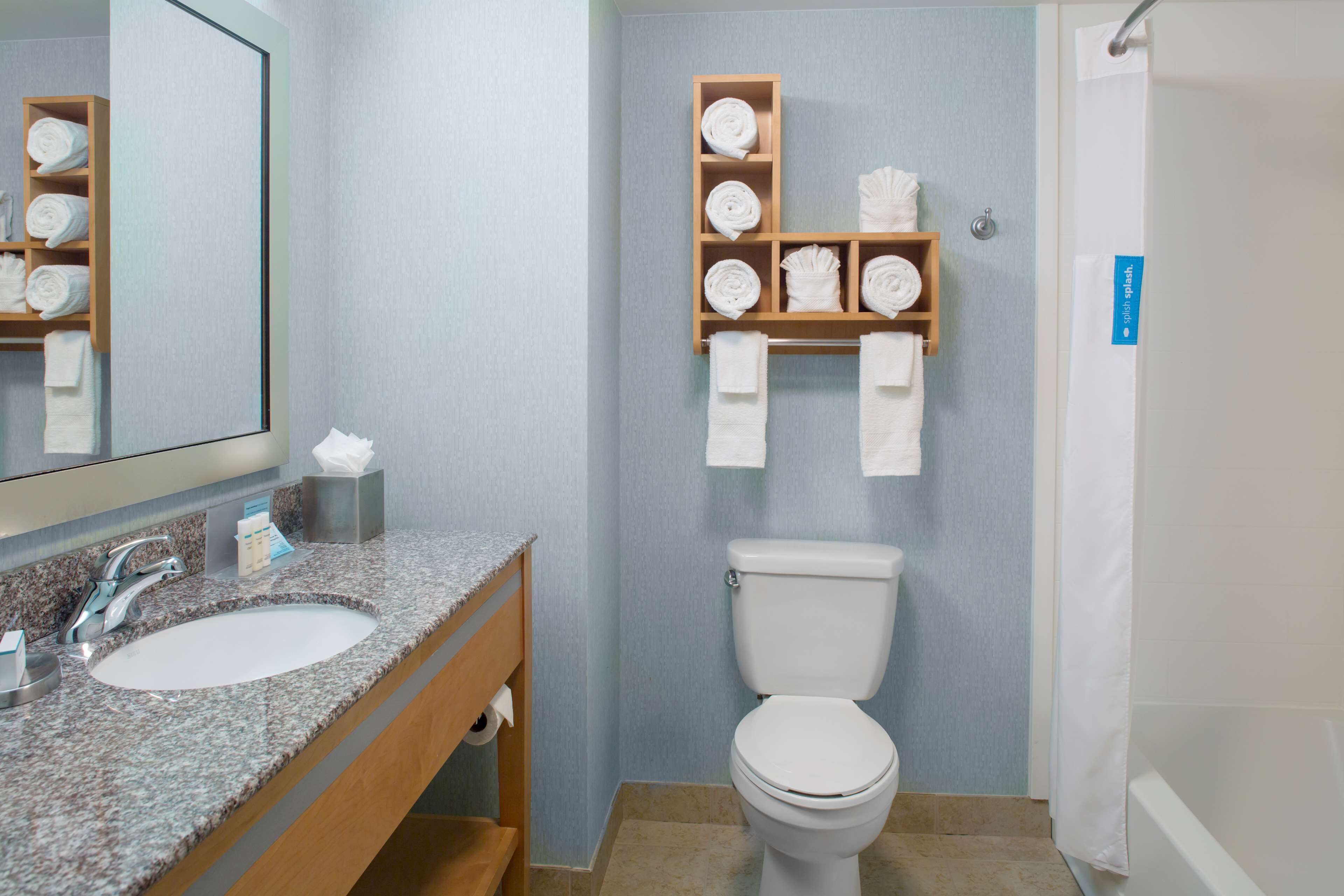 A bathroom with a granite sink, a toilet, and a towel rack with neatly folded towels.