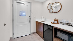 A modern kitchen with a white door, wooden cabinets, a built-in dishwasher, and a microwave. - Hampton Inn & Suites Sarasota/Bradenton-Airport, FL (Sarasota)