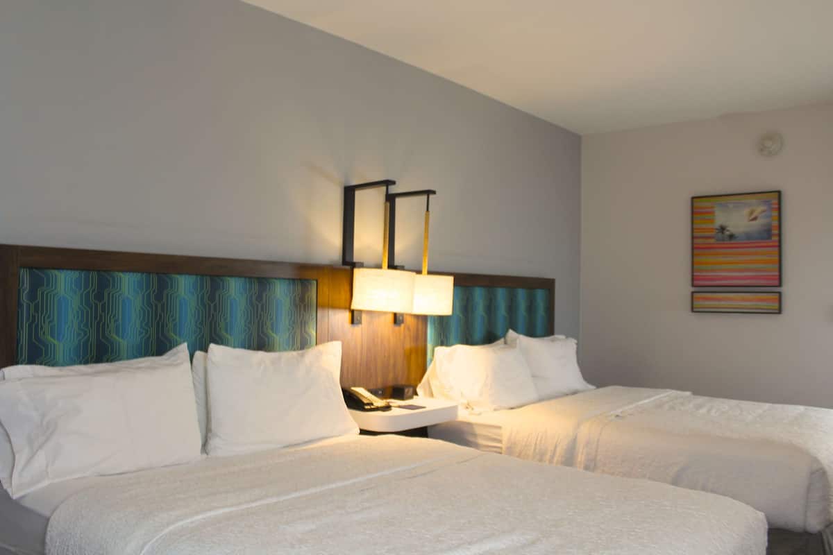 A hotel room with two beds, a nightstand with a lamp, and a painting on the wall.