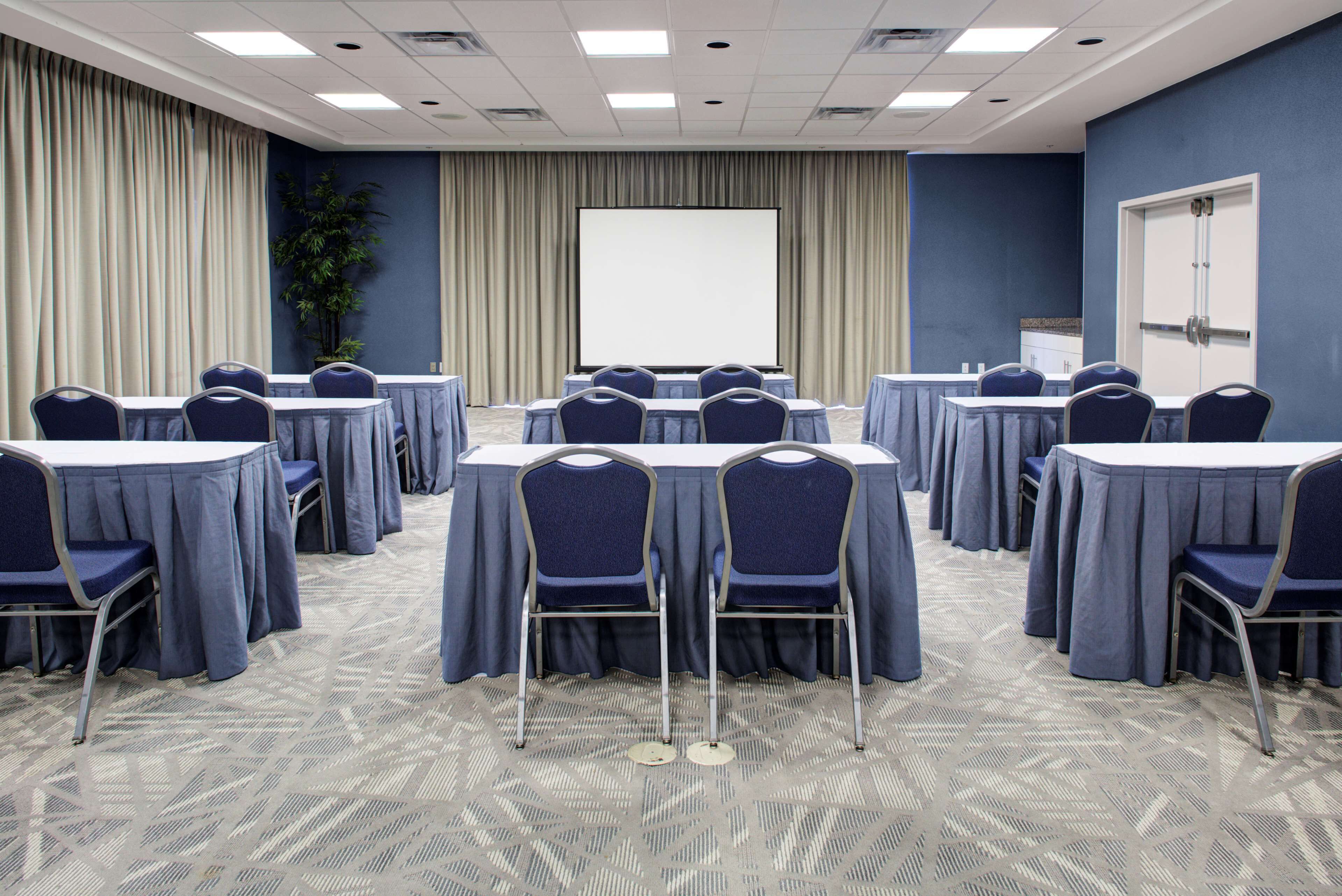 A conference room with round tables, chairs, a projector screen, and a door.