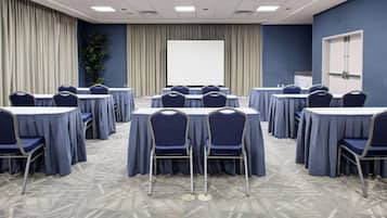 A conference room with round tables, chairs, a projector screen, and a door.