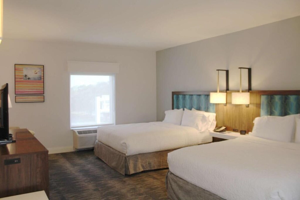 A hotel room with two beds, a desk, a television, and a window with a view.