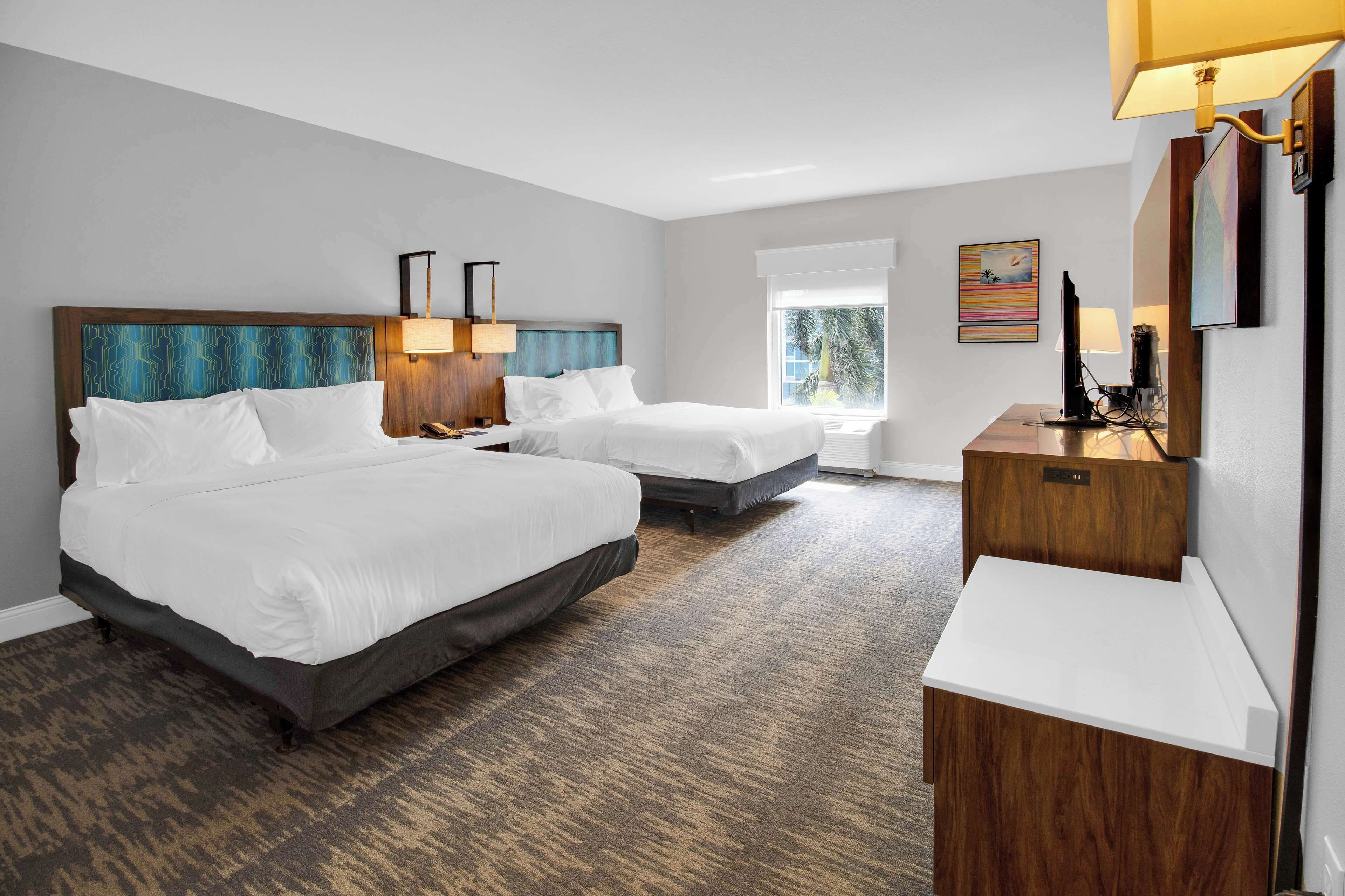 A hotel room with two beds, a desk, and a large window.