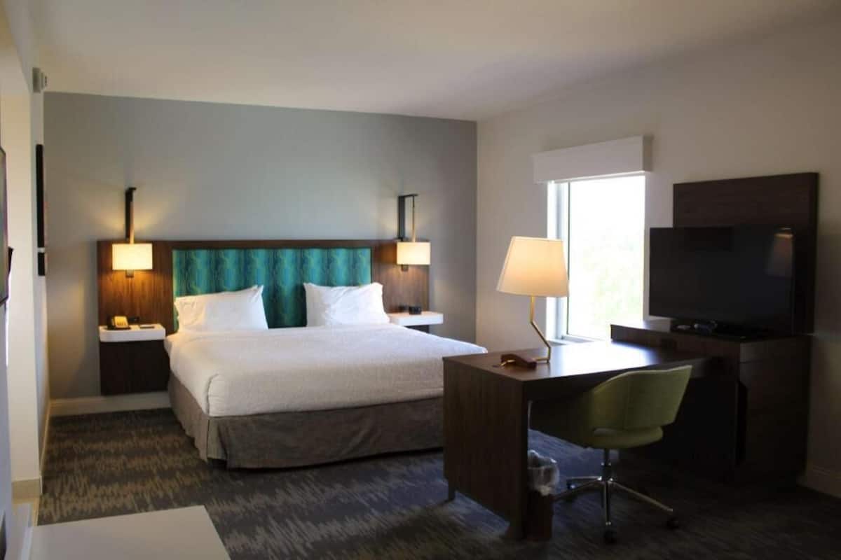 A hotel room with a bed, desk, chair, TV, and lamps.