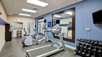 Une salle de sport équipée de tapis de course, de vélos elliptiques et d’une série de haltères.