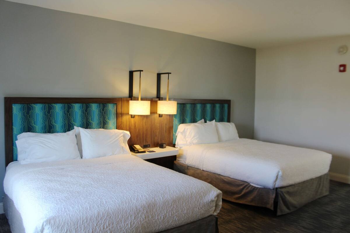A hotel room with two beds, a wooden headboard, a nightstand with a lamp, and a telephone.