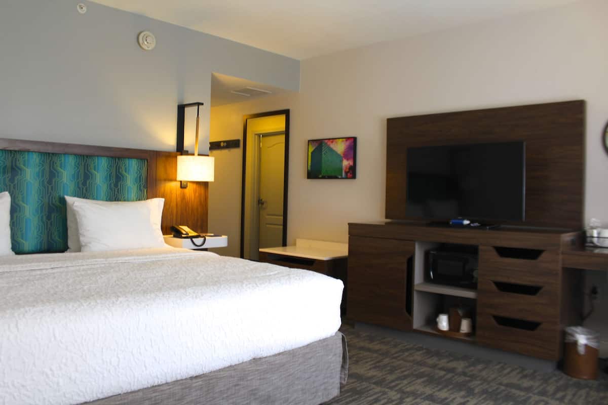 A hotel room with a large bed, a TV, a desk, and a mirror.