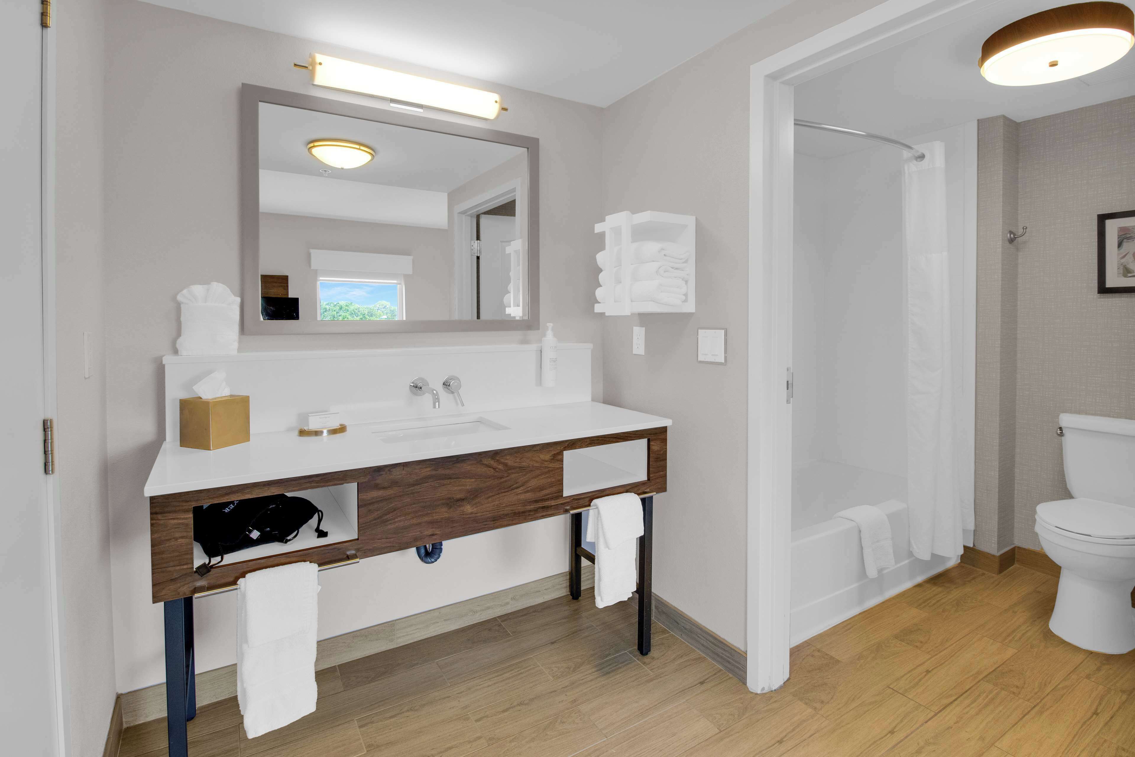 A modern bathroom with a white vanity, a large mirror, a shower, and a toilet.