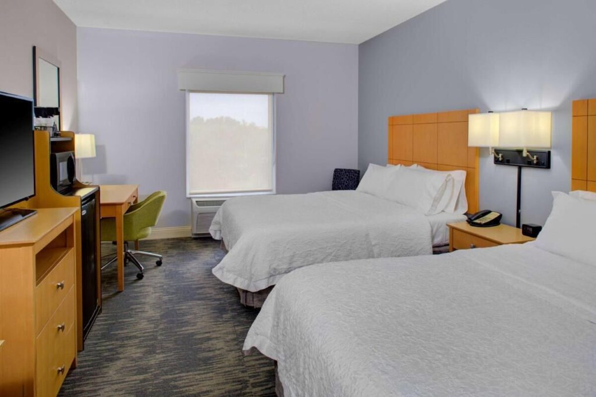 A hotel room with two beds, a desk, a chair, a TV, and a window.
