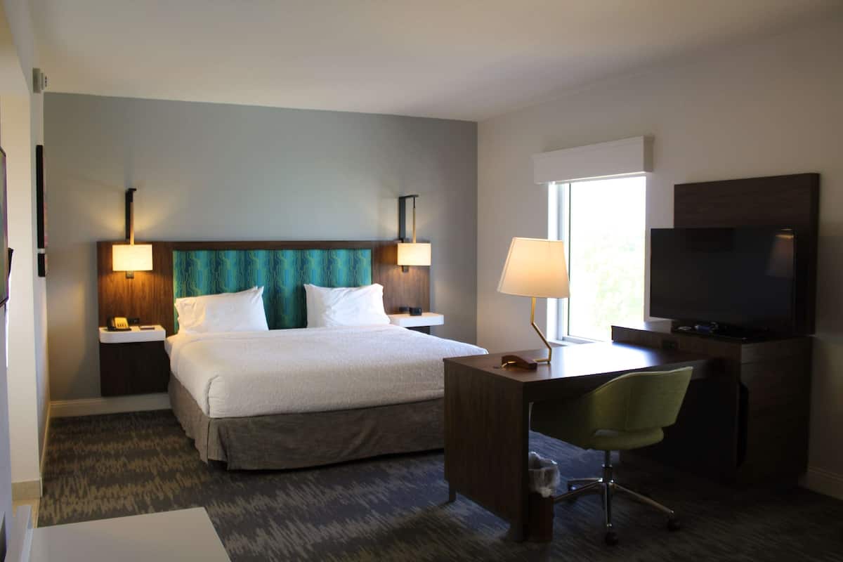 A hotel room with a bed, desk, chair, TV, and two bedside lamps.
