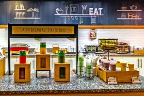 A breakfast bar with a chalkboard sign that reads "HAPPY BREAKFAST STARTS HERE" and a variety of food and drink options. - Hampton Inn & Suites Sarasota/Bradenton-Airport, FL (Sarasota)