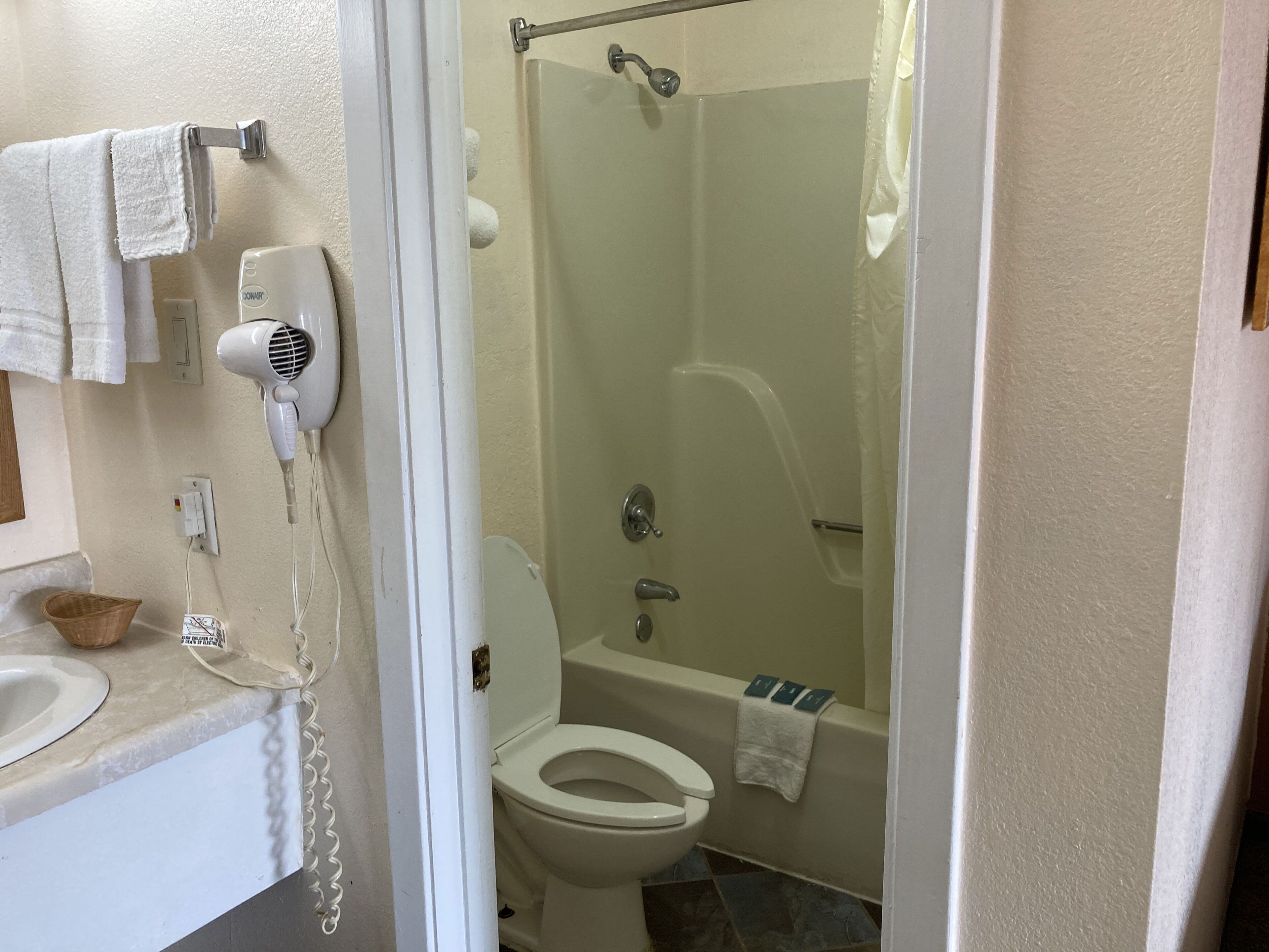 A bathroom with a toilet, a shower, a hairdryer, and a towel rack.