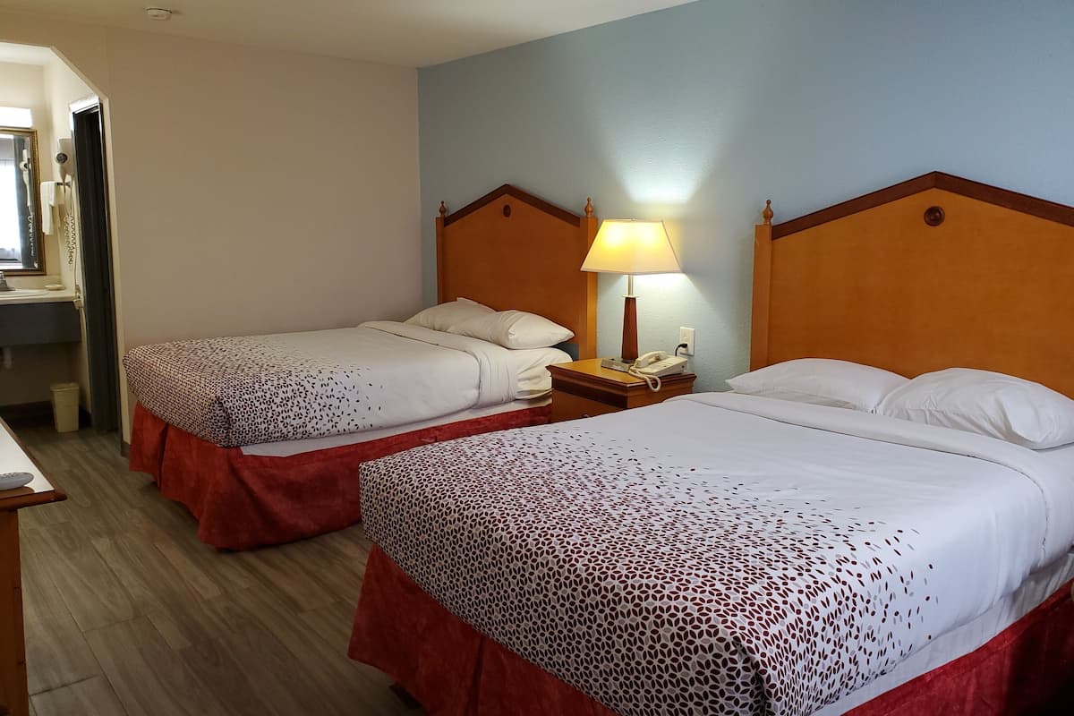 Une chambre d’hôtel avec deux lits, chacun doté d’une tête de lit en bois, d’une table de chevet avec une lampe et d’un téléphone.