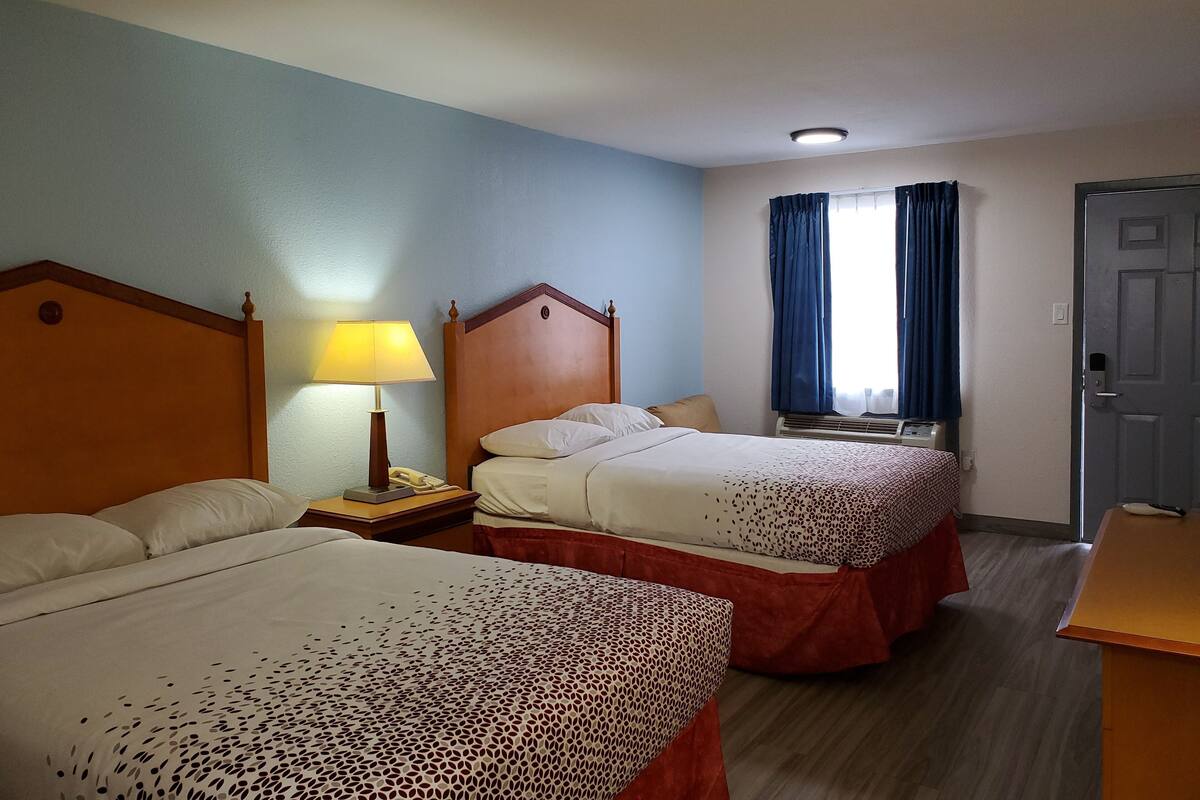 Une chambre d’hôtel avec deux lits, une table de chevet avec une lampe, un téléphone et une fenêtre avec des rideaux.