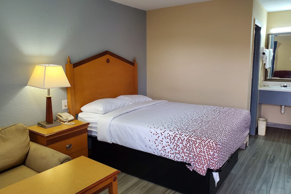 Une chambre d’hôtel comprenant un lit, une table de chevet avec une lampe, un téléphone, une petite table et une chaise.