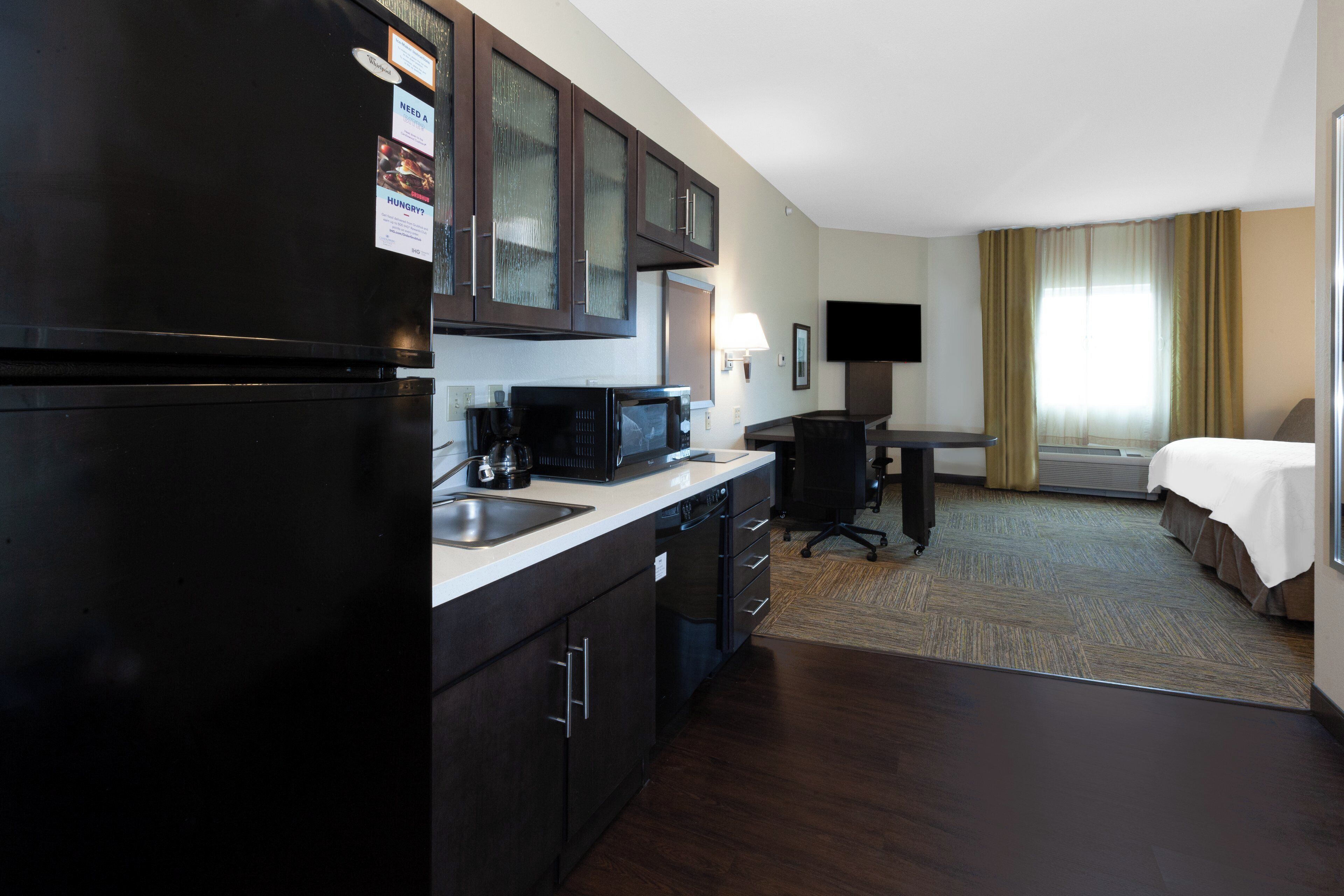 A hotel room with a kitchenette, a bed, a desk, and a television.