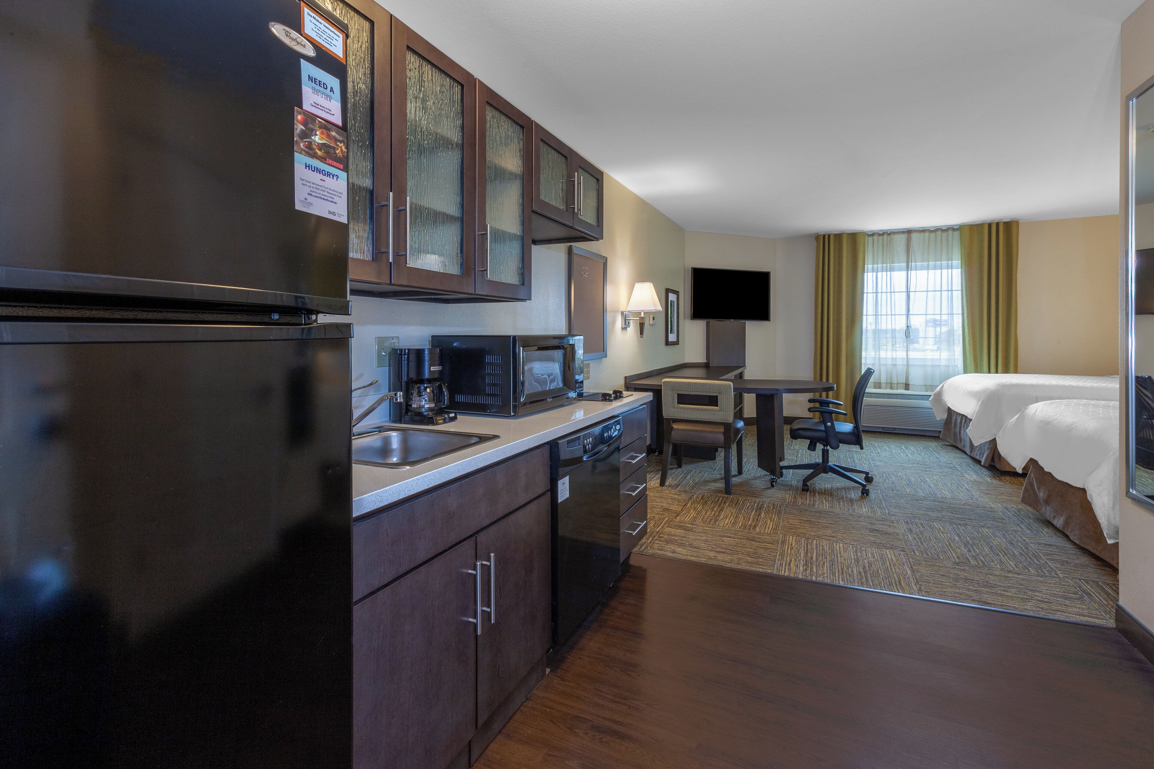 A hotel room with a kitchenette, a bed, a desk, and a TV.