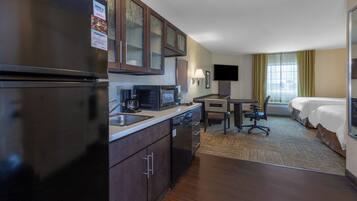 A hotel room with a kitchenette, a bed, a desk, and a TV.