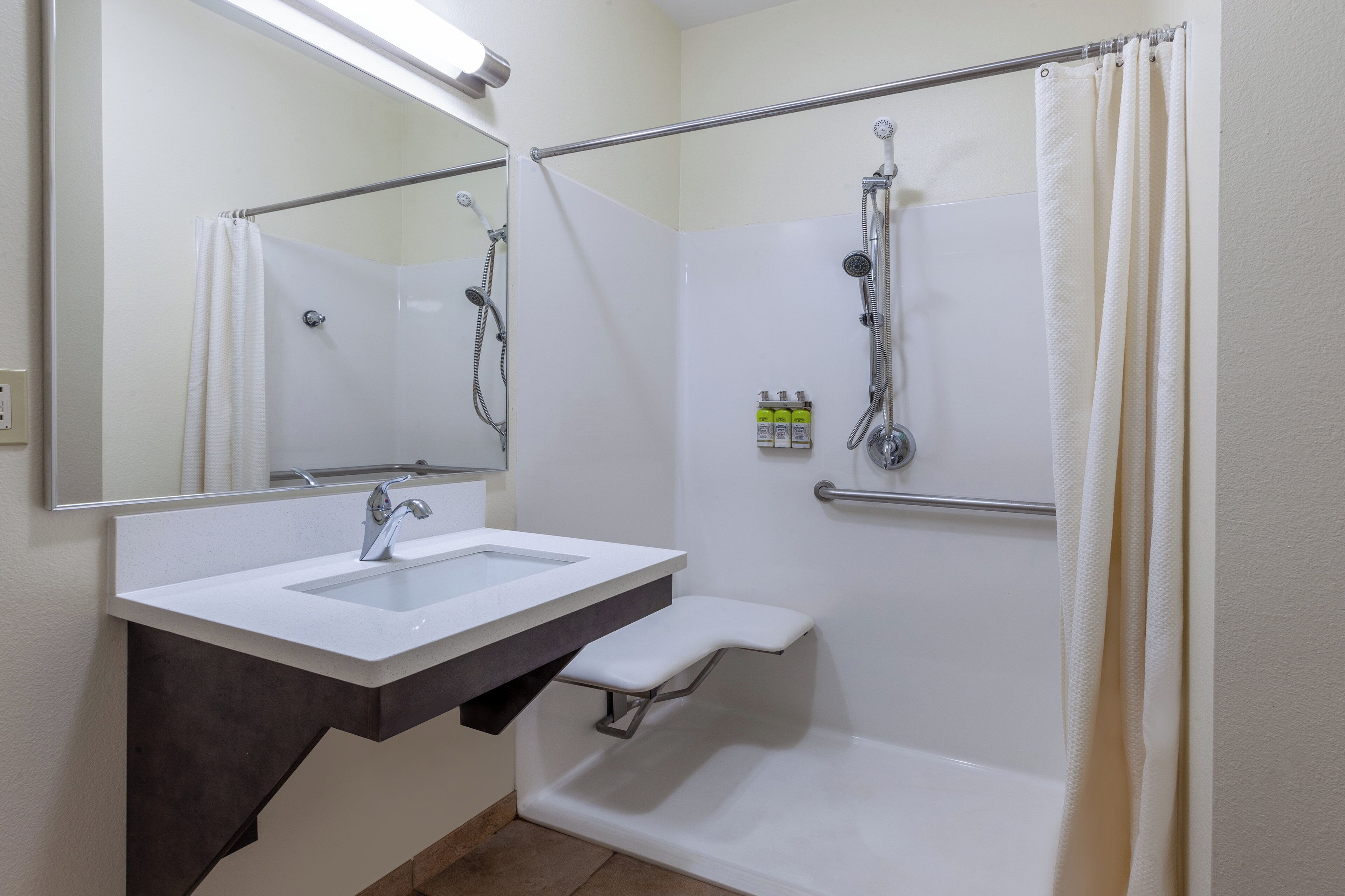 A bathroom with a white sink, a mirror, a shower with a handheld showerhead, and a towel rack.