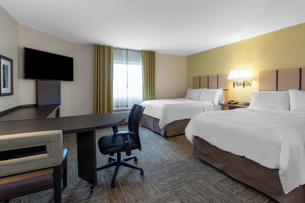 A hotel room with two beds, a desk, a chair, a television, and a window with curtains.